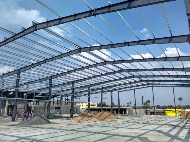 Wide-span PEB roof purlin framework under construction against a blue sky