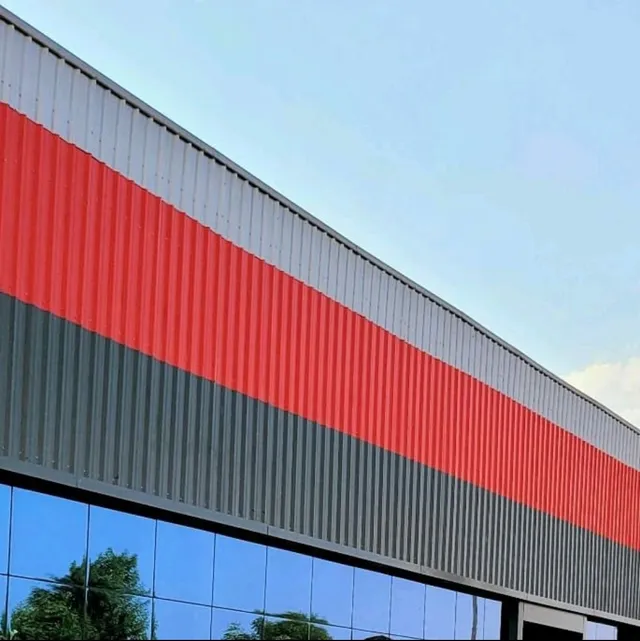 Red and grey profile sheet facade cladding above a glass curtain wall